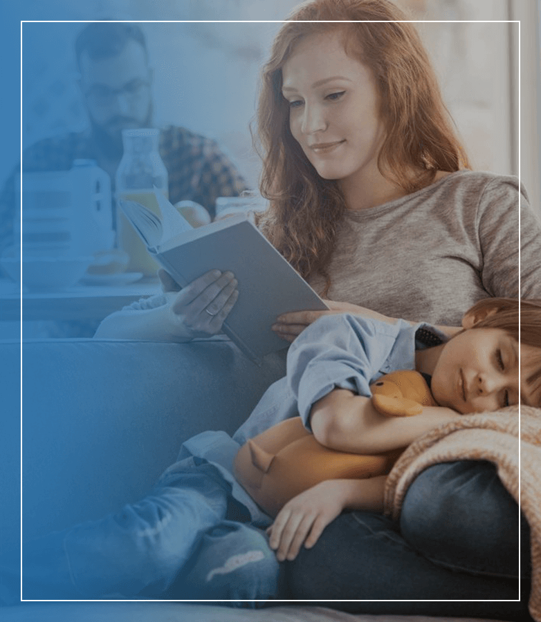 young mother reading book while her child sleeping on her lap